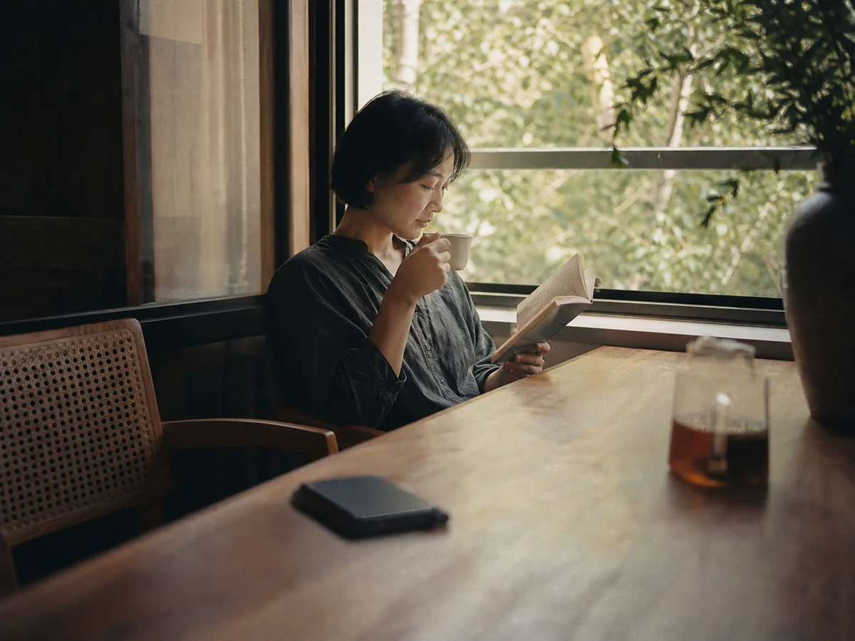 桌上的手机倒扣着而人物在窗边读书喝茶